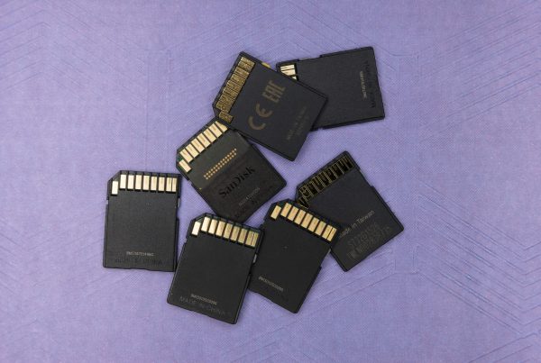 Seven black SD cards scattered on a purple surface with visible gold contacts. The arrangement is casual, evoking a sense of technology and storage.